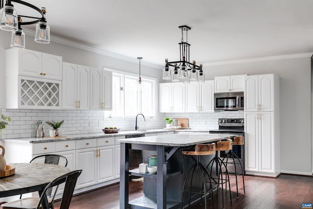 kitchen with decorative light fixtures, a kitchen island, white cabinets, and appliances with stainless steel finishes