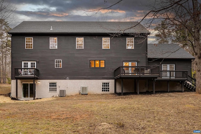 back house at dusk featuring a wooden deck, a yard, and central AC