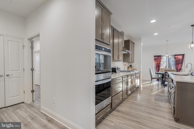 kitchen with dark brown cabinetry, light countertops, light wood-style flooring, appliances with stainless steel finishes, and a sink