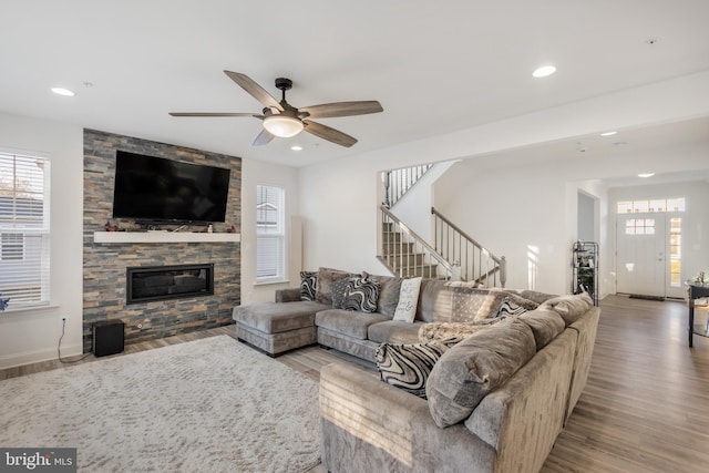 living area with recessed lighting, a stone fireplace, wood finished floors, and stairs