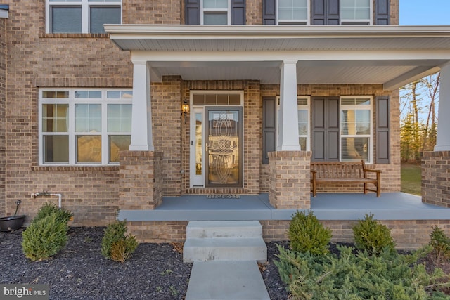 doorway to property featuring covered porch and brick siding