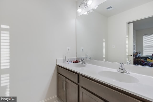 bathroom with double vanity, baseboards, visible vents, and a sink