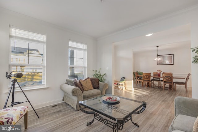 living area featuring visible vents, baseboards, light wood finished floors, crown molding, and a chandelier