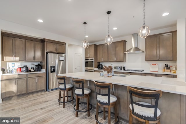 kitchen featuring light wood-style flooring, appliances with stainless steel finishes, wall chimney exhaust hood, and a kitchen breakfast bar