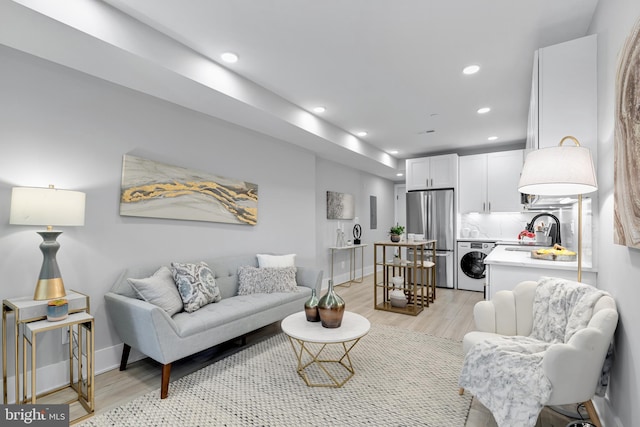 living room with washer / dryer, sink, and light hardwood / wood-style flooring