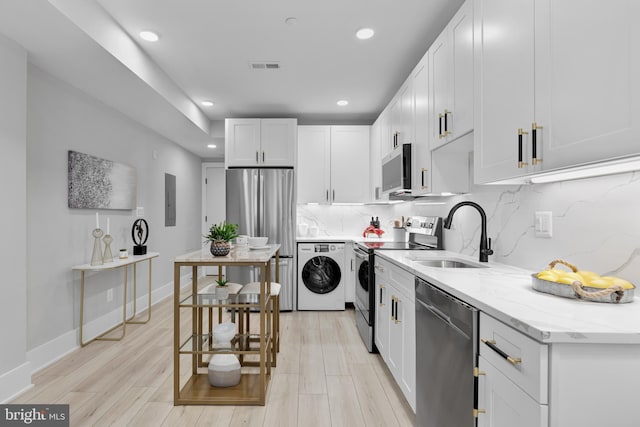 kitchen featuring appliances with stainless steel finishes, sink, white cabinets, backsplash, and light stone countertops