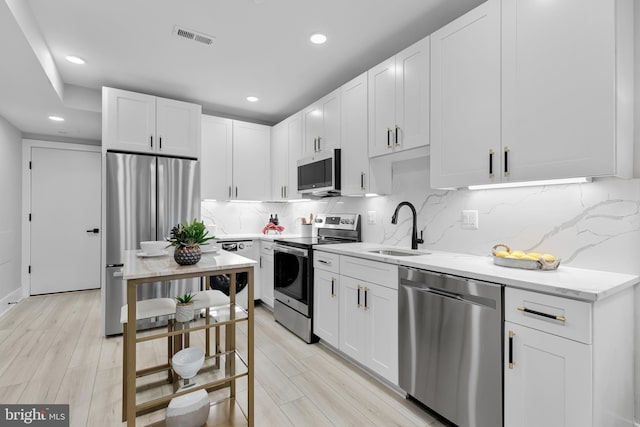 kitchen with white cabinetry, sink, light stone counters, and appliances with stainless steel finishes