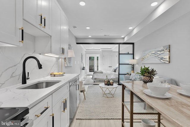 kitchen featuring dishwasher, white cabinetry, sink, decorative backsplash, and light stone counters