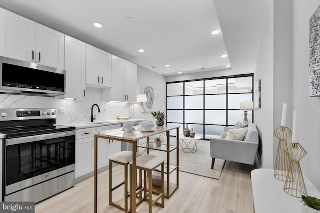 kitchen featuring appliances with stainless steel finishes, sink, white cabinets, decorative backsplash, and light hardwood / wood-style floors