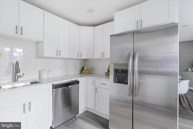 kitchen with sink, appliances with stainless steel finishes, backsplash, white cabinets, and light wood-type flooring