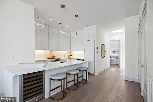 kitchen featuring a breakfast bar, beverage cooler, white cabinetry, dark hardwood / wood-style flooring, and hanging light fixtures