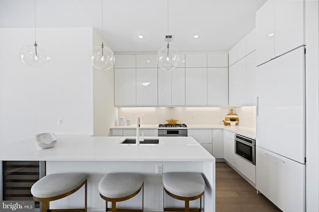 kitchen with hanging light fixtures, white cabinets, beverage cooler, sink, and oven