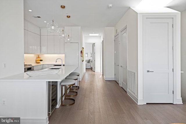 kitchen with kitchen peninsula, sink, white cabinets, a kitchen breakfast bar, and pendant lighting