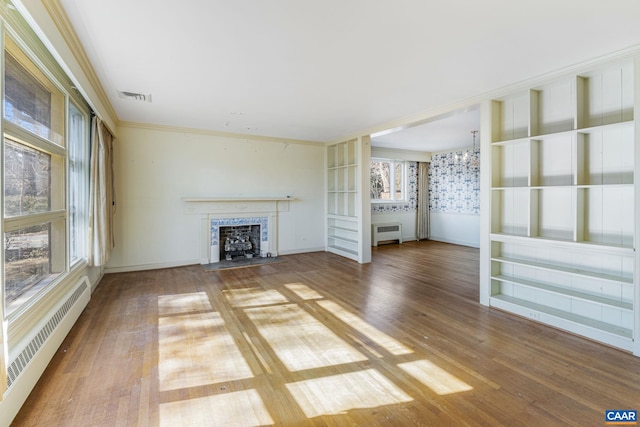 unfurnished living room with an inviting chandelier, wood-type flooring, a baseboard radiator, ornamental molding, and radiator