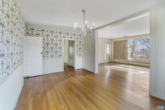 unfurnished dining area with hardwood / wood-style floors, crown molding, a notable chandelier, and radiator