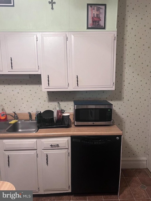 kitchen with dark tile patterned floors, black dishwasher, sink, and white cabinets