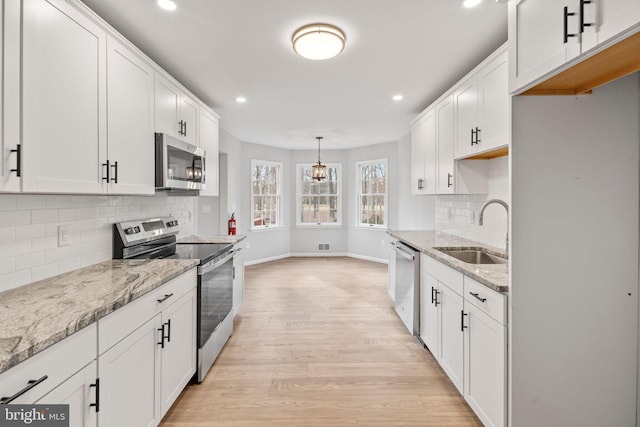 kitchen featuring stainless steel appliances, sink, white cabinets, and decorative light fixtures