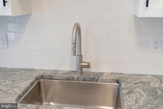 interior details with sink, white cabinets, and stone counters