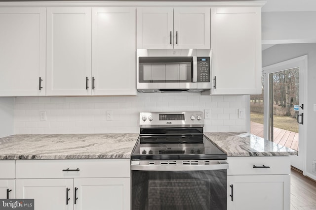 kitchen with white cabinetry, stainless steel appliances, light stone countertops, hardwood / wood-style floors, and decorative backsplash