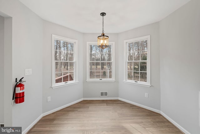 unfurnished dining area with a wealth of natural light, light hardwood / wood-style floors, and a chandelier