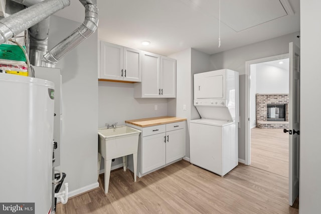 laundry area featuring gas water heater, stacked washer and clothes dryer, light hardwood / wood-style floors, and a brick fireplace