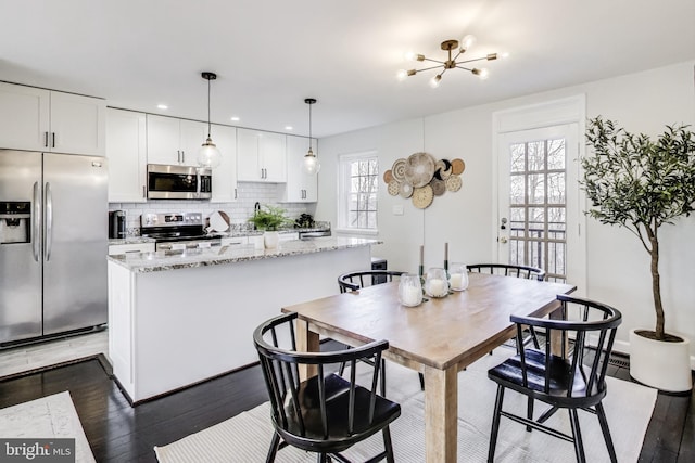 kitchen with appliances with stainless steel finishes, hanging light fixtures, light stone counters, a center island, and white cabinetry