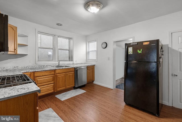 kitchen with sink, black fridge, light stone counters, light hardwood / wood-style flooring, and stainless steel dishwasher