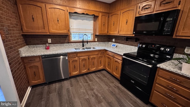 kitchen featuring sink, light stone counters, black appliances, brick wall, and dark hardwood / wood-style flooring