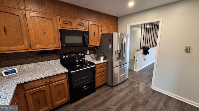 kitchen with light stone countertops, decorative backsplash, black appliances, and dark hardwood / wood-style floors