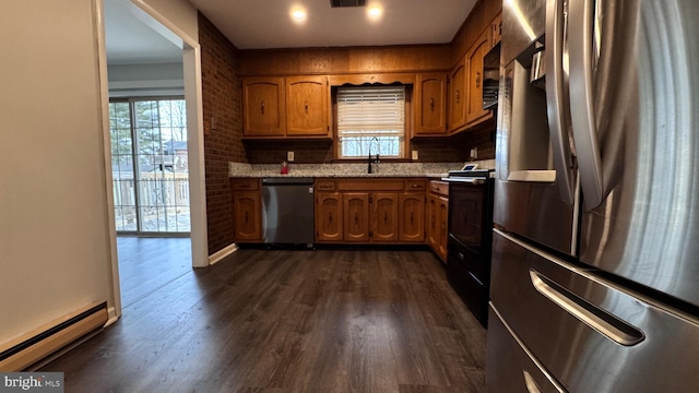 kitchen featuring dark wood-type flooring, sink, light stone counters, baseboard heating, and appliances with stainless steel finishes