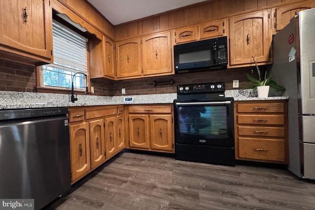 kitchen featuring sink, tasteful backsplash, light stone counters, dark hardwood / wood-style floors, and black appliances