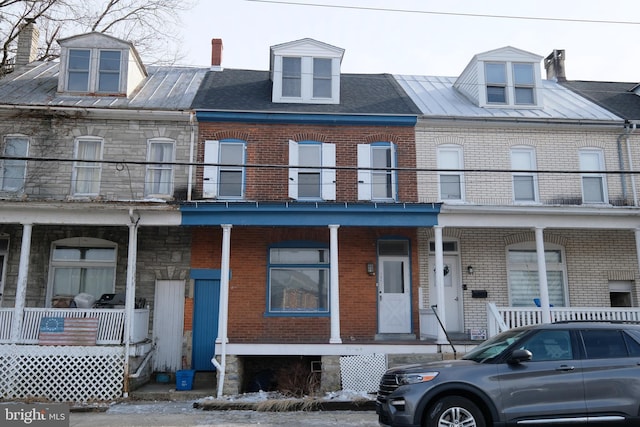 view of property featuring a porch, stone siding, brick siding, and a balcony