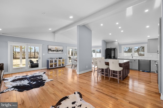 living room featuring a healthy amount of sunlight, vaulted ceiling with beams, sink, and light hardwood / wood-style flooring