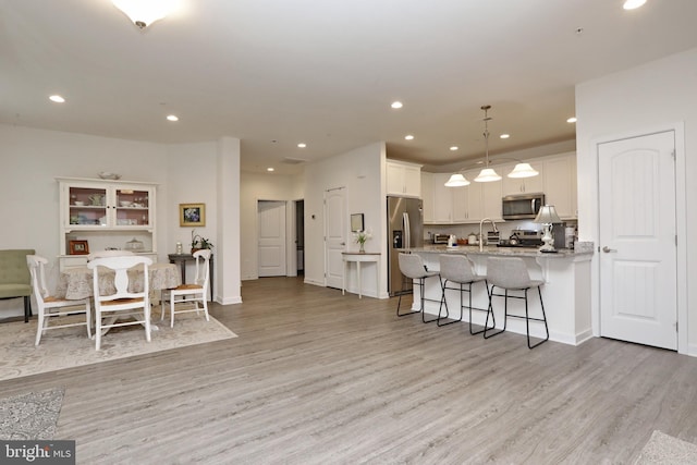 kitchen with a breakfast bar area, decorative light fixtures, light hardwood / wood-style flooring, appliances with stainless steel finishes, and white cabinets