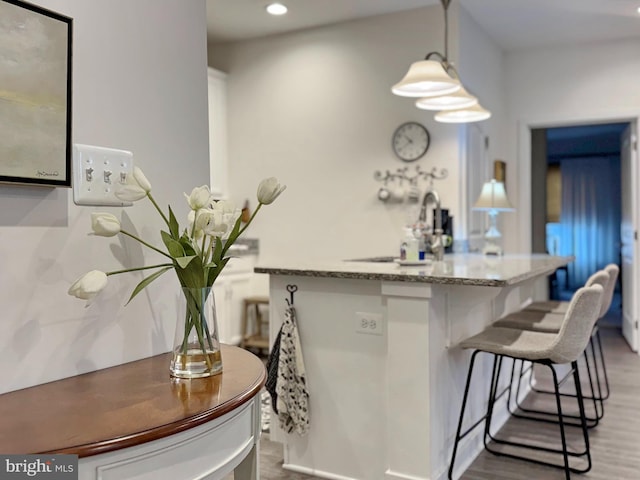 kitchen featuring white cabinetry, hardwood / wood-style floors, decorative light fixtures, and light stone countertops