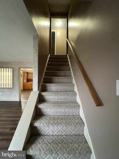 stairs with wood-type flooring and a textured ceiling