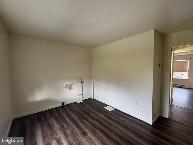 empty room with a baseboard heating unit and dark hardwood / wood-style floors