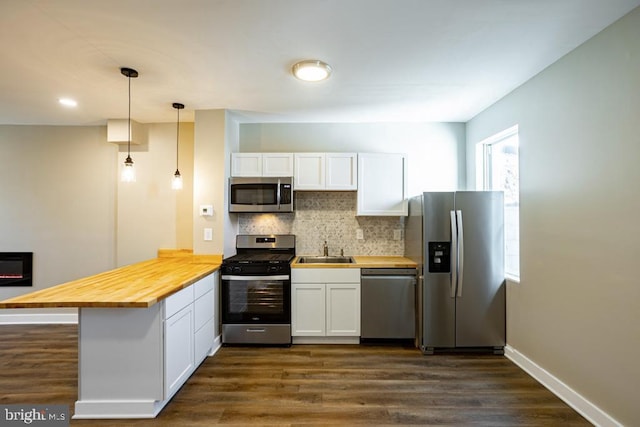 kitchen with wood counters, white cabinetry, hanging light fixtures, appliances with stainless steel finishes, and kitchen peninsula