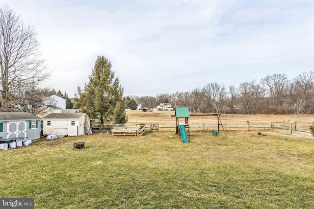 view of yard with a playground, an outdoor fire pit, a rural view, and a storage shed