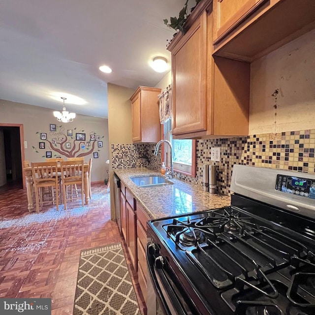 kitchen featuring appliances with stainless steel finishes, sink, backsplash, a notable chandelier, and light stone countertops