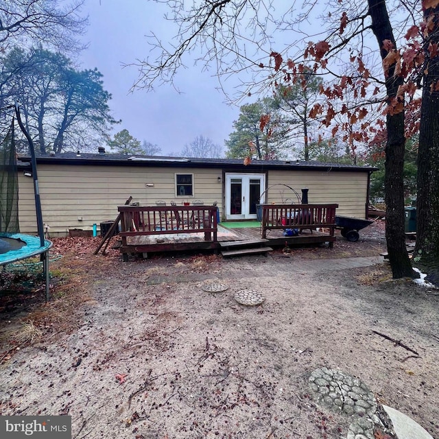 rear view of house with french doors, a deck, and a trampoline