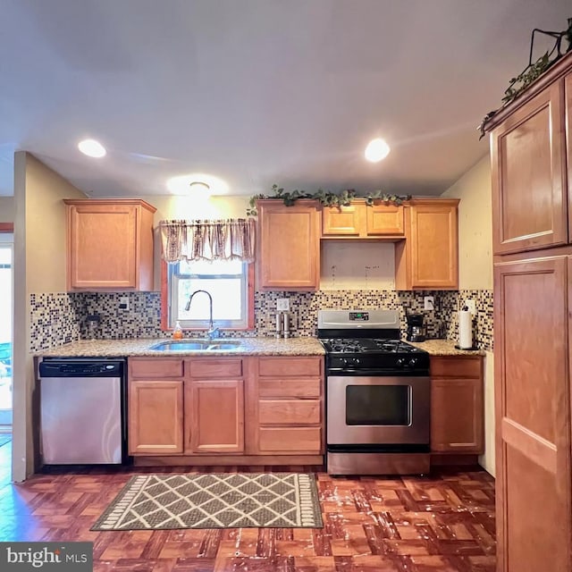 kitchen with dark parquet flooring, sink, stainless steel appliances, light stone countertops, and backsplash