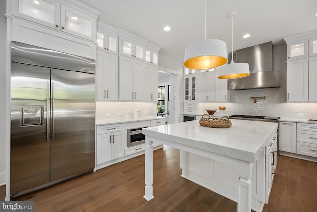 kitchen with wall chimney exhaust hood, stainless steel built in refrigerator, white cabinetry, pendant lighting, and wall oven