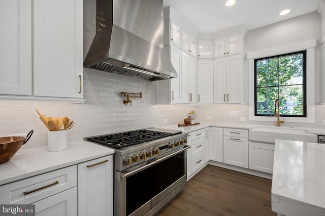 kitchen with high end stainless steel range oven, white cabinetry, sink, and wall chimney exhaust hood