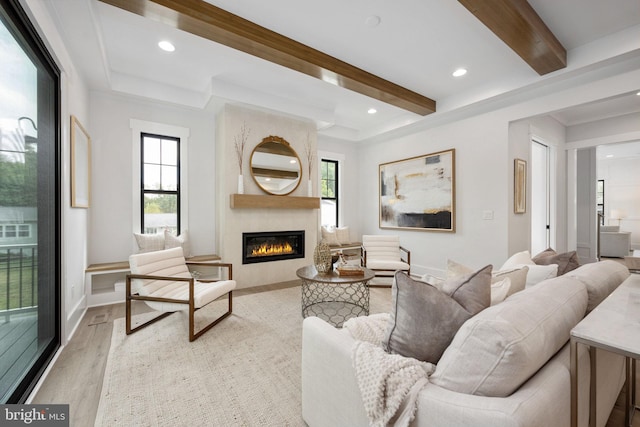 living room featuring a fireplace, beamed ceiling, light hardwood / wood-style floors, and a healthy amount of sunlight