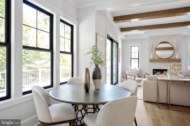 dining room with a fireplace, light hardwood / wood-style floors, and beamed ceiling