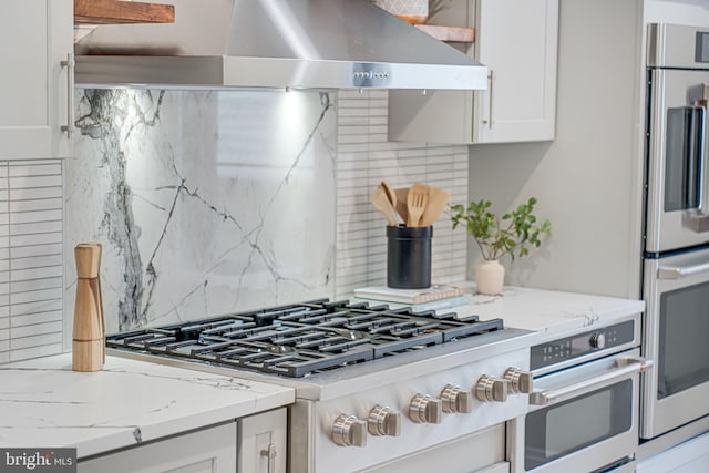 kitchen with backsplash, fridge, light stone counters, white cabinets, and exhaust hood