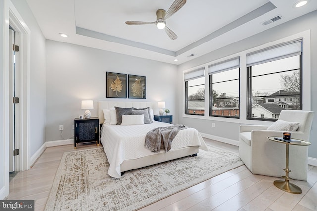 bedroom featuring ceiling fan, light hardwood / wood-style floors, and a tray ceiling