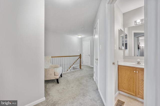 hall featuring light carpet, a sink, visible vents, and baseboards