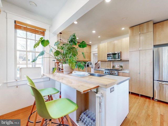 kitchen with sink, a breakfast bar area, appliances with stainless steel finishes, light hardwood / wood-style floors, and light brown cabinetry